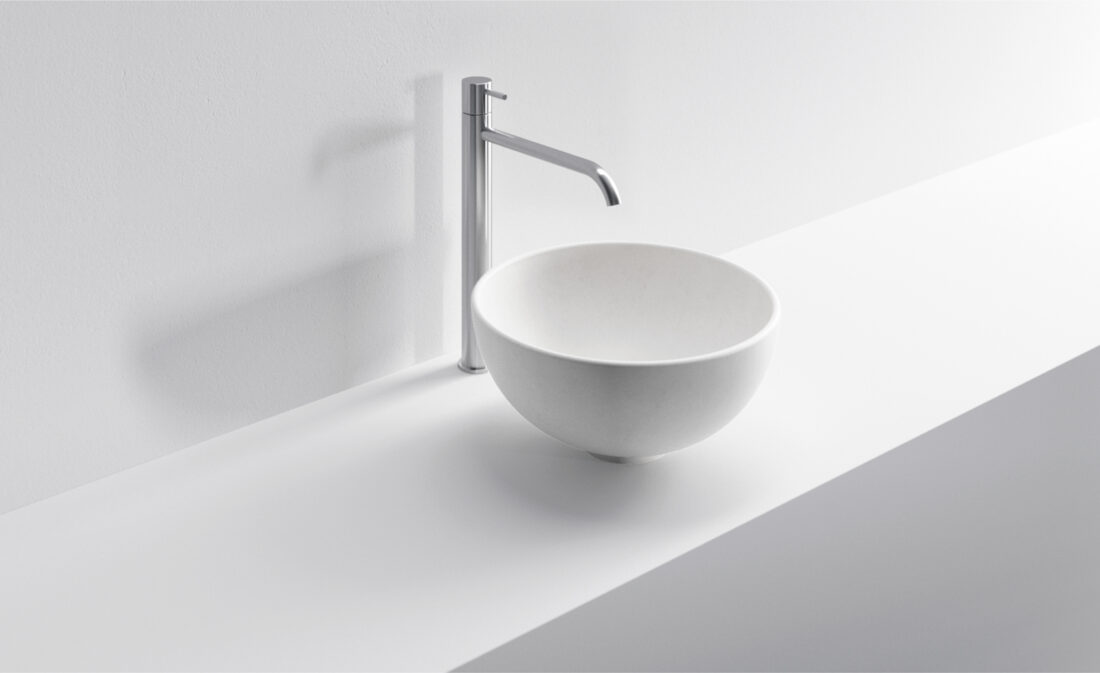 Lavabo rotondo bianco con rubinetto in stile minimalista su superficie bianca.