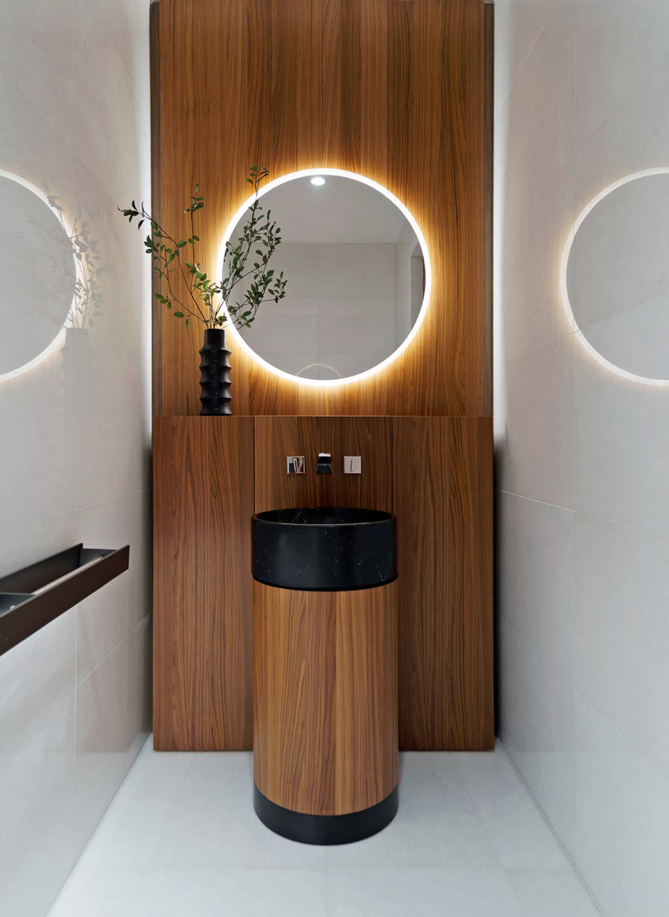 Immagine di un solido mobile lavabo con specchio tondo illuminato in un ambiente moderno.