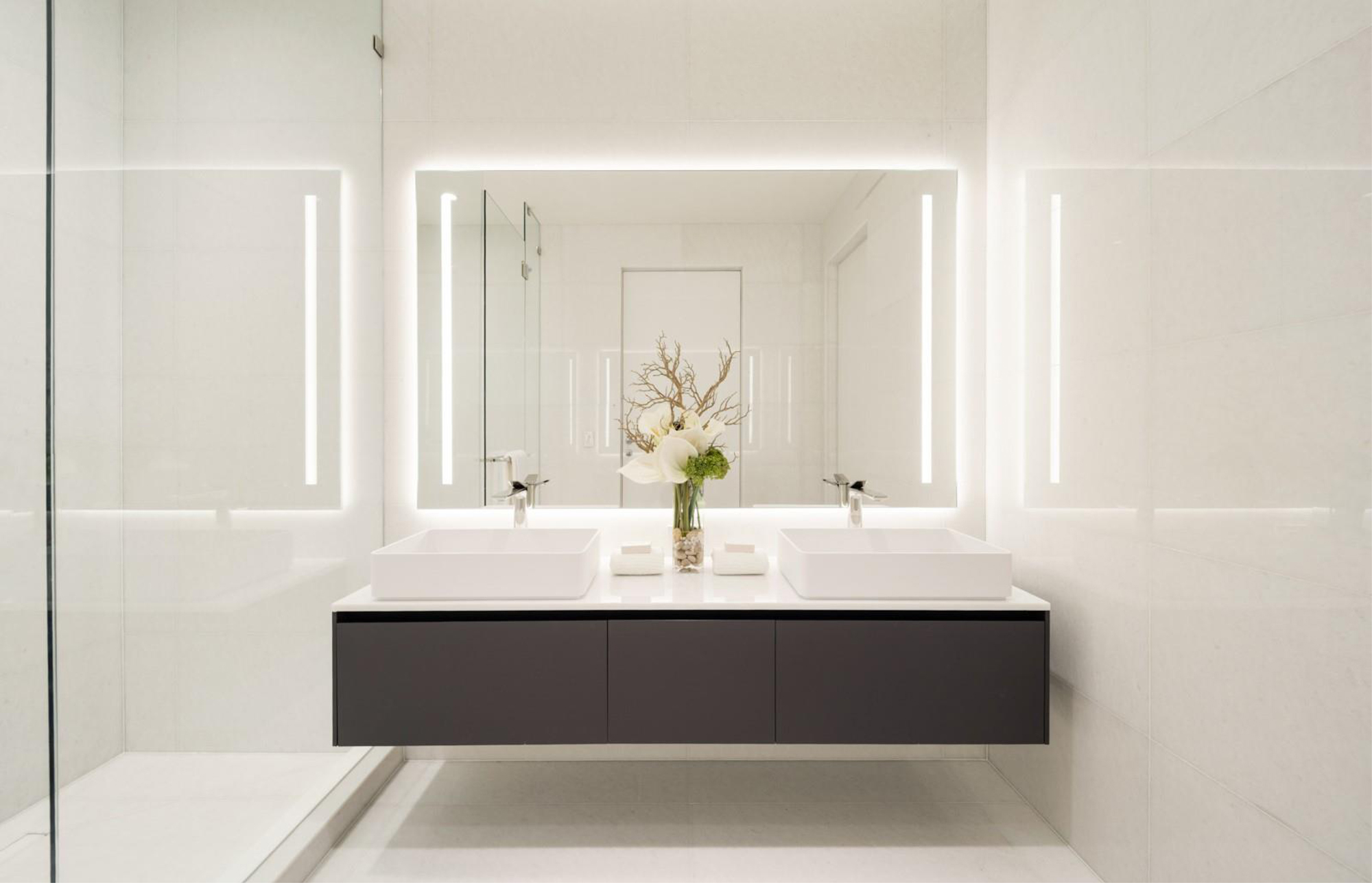 Bagno luminoso con lavabo doppi e specchi verticali illuminati.